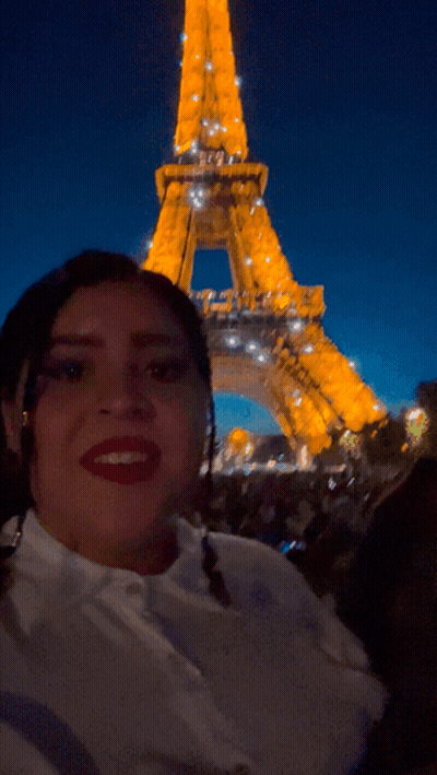 A Woman Taking A Picture In Front Of The Eiffel Tower At Night GIF
