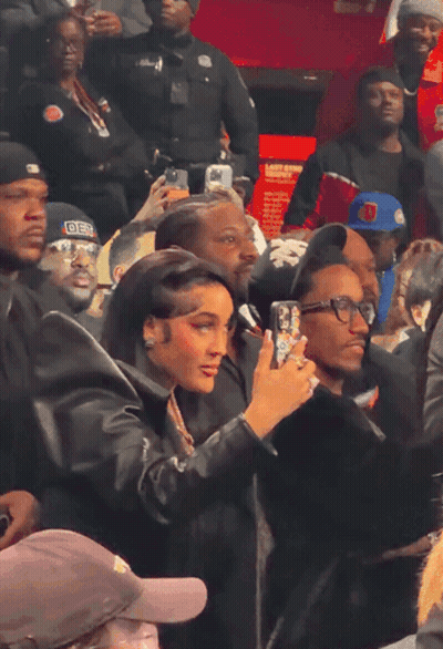 A Woman Taking A Picture Of A Man Wearing A Hat That Says ' Der ' On It GIF