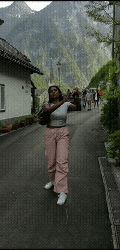 A Woman Taking A Picture Of A Mountain While Standing On A Street GIF