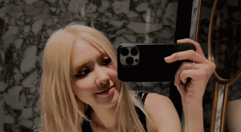 A Woman Taking A Picture Of Herself In A Mirror With Her Phone GIF