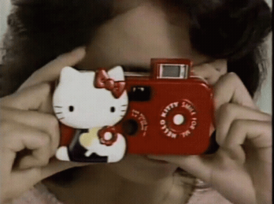 A Woman Taking A Picture With A Red Hello Kitty Camera GIF