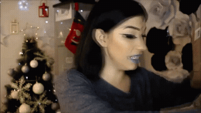 A Woman Taking A Selfie With A Christmas Tree In The Background GIF