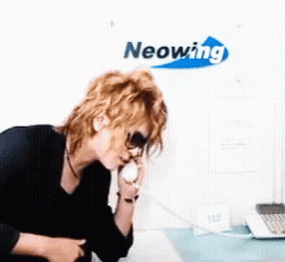 A Woman Talking On A Phone In Front Of A Neonwing Sign GIF