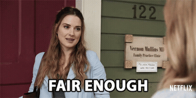 A Woman Talking To Another Woman In Front Of A Sign For Vernon Mullins Md GIF