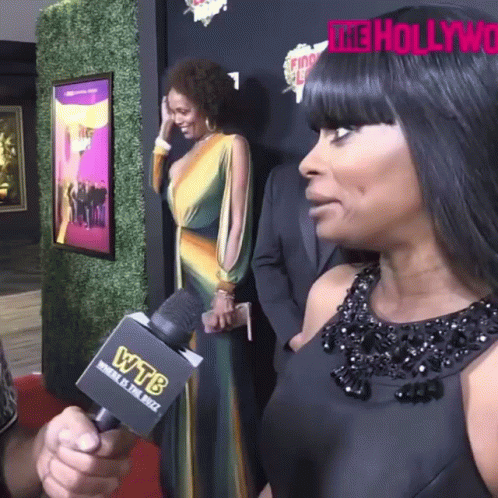 A Woman Talks Into A Wtb Microphone While Standing On A Red Carpet GIF