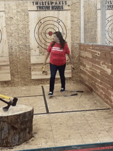 A Woman Throws An Axe In Front Of A Twisted Axes Throw House Sign GIF