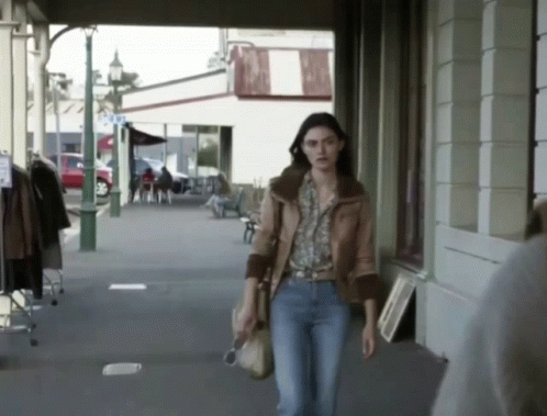 A Woman Walking Down A Sidewalk In Front Of A Store That Says ' A & A ' On It GIF