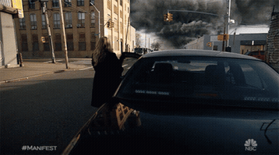 A Woman Walking Down A Street Next To A Car That Says Nbc On It GIF