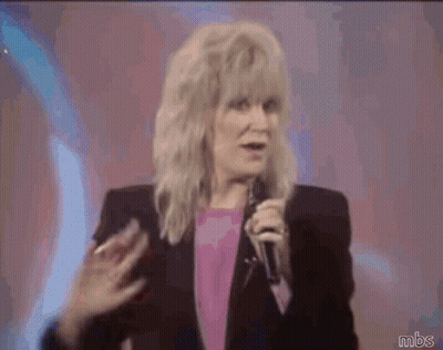 A Woman Waving Her Hand While Holding A Microphone With Mbs Written Below Her GIF