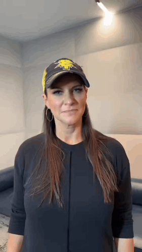 A Woman Wearing A Baseball Cap And A Black Shirt Is Making A Face . GIF