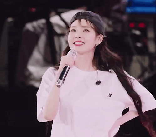 A Woman Wearing A Baseball Cap And A White Shirt Is Holding A Microphone And Smiling GIF