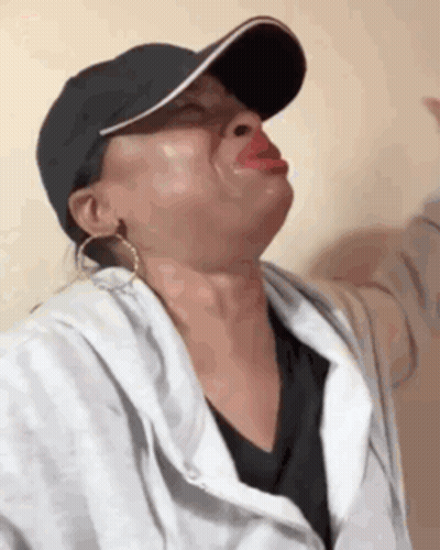 A Woman Wearing A Baseball Cap And Earrings Is Making A Face . GIF