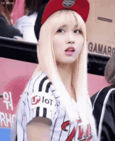 A Woman Wearing A Baseball Uniform And A Red Hat Is Standing In A Crowd . GIF