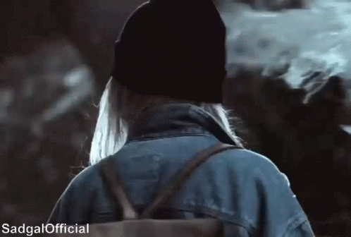 A Woman Wearing A Beanie And A Denim Jacket Is Walking With A Backpack .. GIF