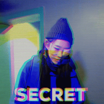 A Woman Wearing A Beanie And Sunglasses Is Standing In Front Of The Word Secret GIF