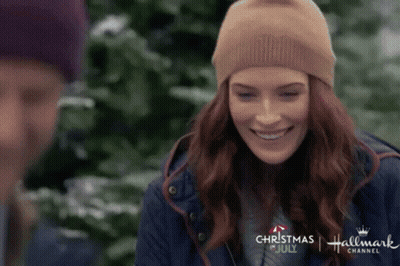 A Woman Wearing A Beanie Is Smiling In Front Of A Man In A Blue Jacket . GIF