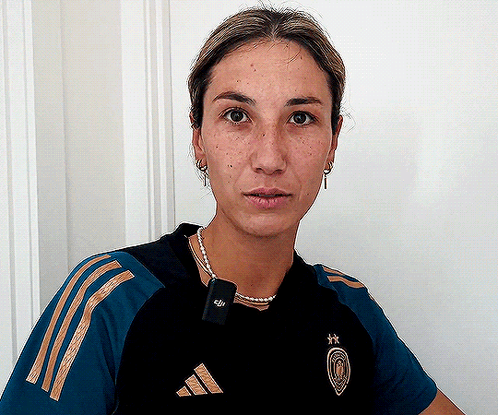 A Woman Wearing A Black And Gold Adidas Shirt Looks At The Camera GIF