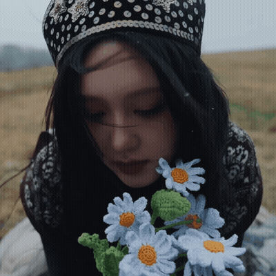 A Woman Wearing A Black And White Polka Dot Hat Holds A Bouquet Of Crocheted Daisies GIF