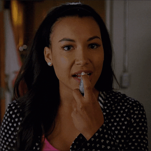A Woman Wearing A Black And White Polka Dot Shirt Is Applying Lipstick To Her Lips GIF