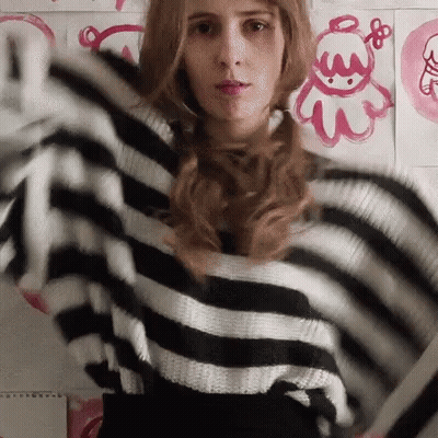 A Woman Wearing A Black And White Striped Sweater Is Standing In Front Of A Wall With Pink Drawings On It GIF
