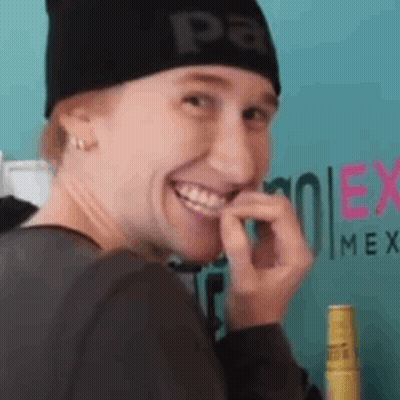 A Woman Wearing A Black Beanie Is Smiling And Biting Her Finger . GIF