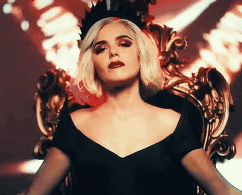 A Woman Wearing A Black Dress And A Crown Is Sitting On A Throne GIF
