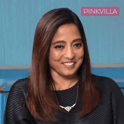 A Woman Wearing A Black Dress And A Necklace Is Smiling In Front Of A Pinkvilla Banner GIF