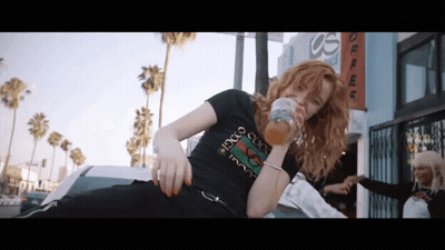 A Woman Wearing A Black Gucci T-Shirt Drinks From A Glass GIF