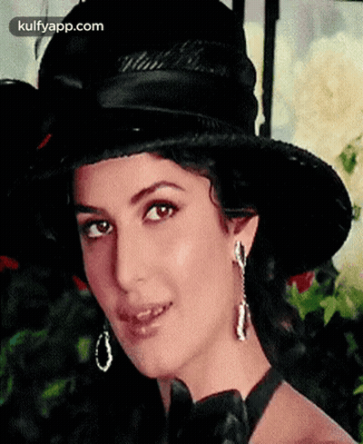 A Woman Wearing A Black Hat And Earrings Is Smiling For The Camera . GIF