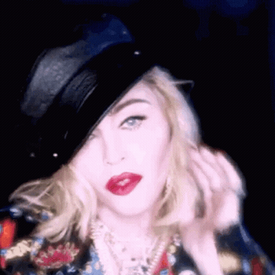 A Woman Wearing A Black Hat And Red Lipstick Is Looking At The Camera . GIF