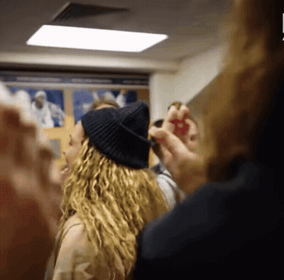 A Woman Wearing A Black Hat Is Standing In A Crowd Of People GIF
