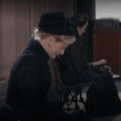 A Woman Wearing A Black Hat Sits In A Chair GIF