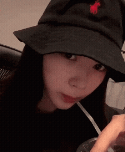 A Woman Wearing A Black Hat With A Red Horse On It Is Drinking Through A Straw . GIF