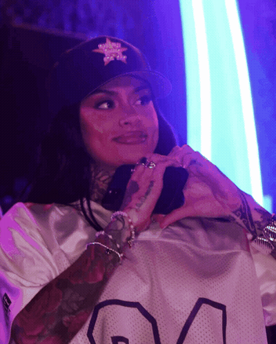 A Woman Wearing A Black Hat With A Star On It Is Making A Heart Shape With Her Hands GIF