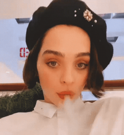 A Woman Wearing A Black Hat With Pearls On It Blowing A Kiss GIF