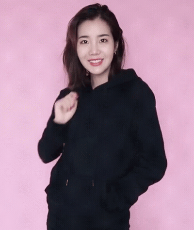 A Woman Wearing A Black Hoodie And A Black Hat Against A Pink Background GIF