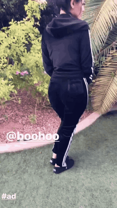 A Woman Wearing A Black Hoodie And Black Pants Is Standing On A Grassy Field GIF