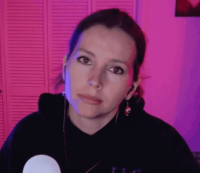 A Woman Wearing A Black Hoodie And Earbuds Looks At The Camera With A Serious Look On Her Face GIF