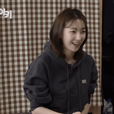 A Woman Wearing A Black Hoodie Smiles In Front Of A Checkered Tablecloth GIF