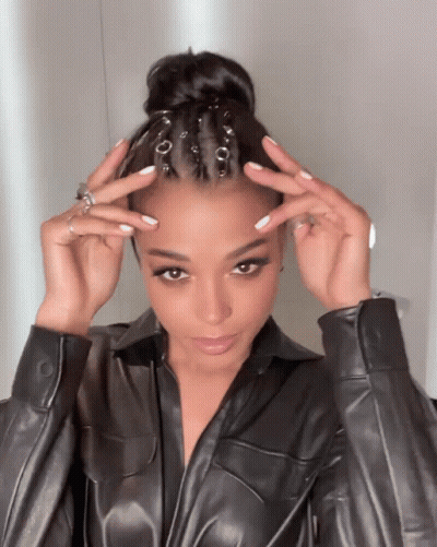 A Woman Wearing A Black Leather Jacket Holds Her Hair Up In A Bun GIF