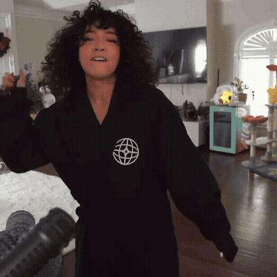 A Woman Wearing A Black Robe With A White Globe On The Front GIF