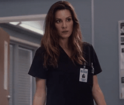 A Woman Wearing A Black Scrub Top Has A Name Tag On Her Chest That Says ' Nurse ' GIF