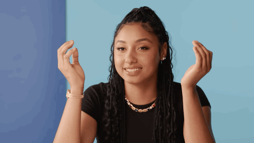 A Woman Wearing A Black Shirt And A Gold Necklace Is Smiling With Her Hands In The Air GIF