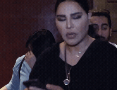 A Woman Wearing A Black Shirt And A Necklace Looks At The Camera GIF