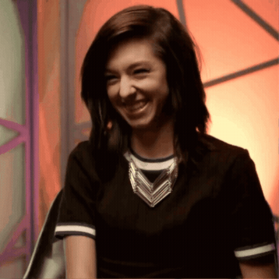A Woman Wearing A Black Shirt And A Necklace Smiles For The Camera GIF