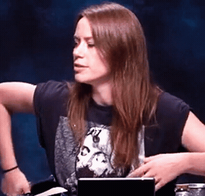 A Woman Wearing A Black Shirt With A Picture Of A Skull On It Is Sitting At A Table With A Laptop . GIF