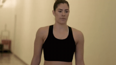 A Woman Wearing A Black Sports Bra Is Walking Down A Hallway GIF