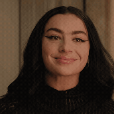 A Woman Wearing A Black Sweater And Hoop Earrings Smiles For The Camera GIF