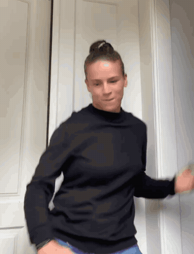 A Woman Wearing A Black Sweater Is Dancing In Front Of A Door GIF