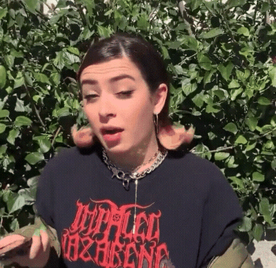 A Woman Wearing A Black T-Shirt And A Necklace Is Standing In Front Of A Tree . GIF